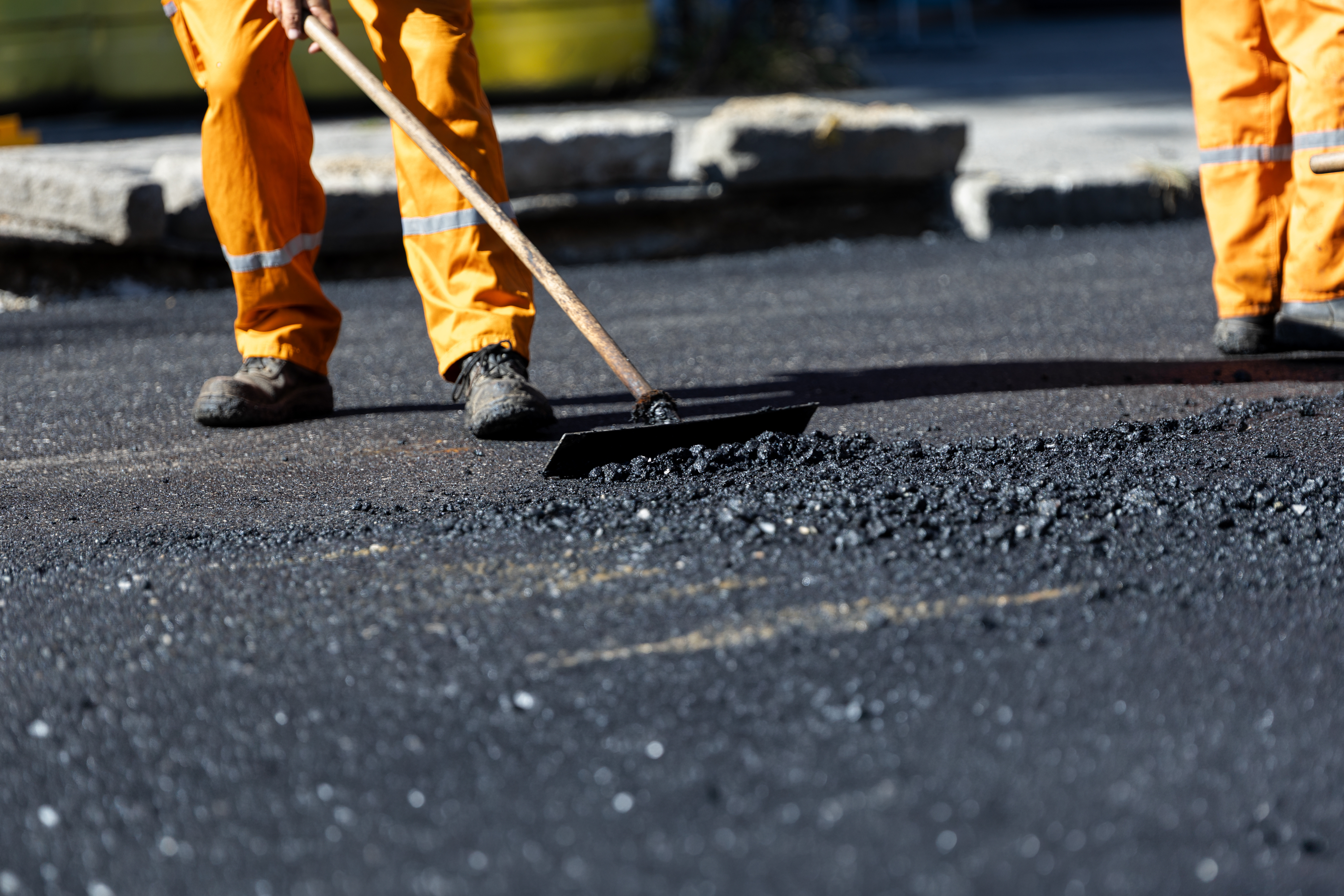 Road workers in yellow safety gear spreading asphalt with hand tools during paving work