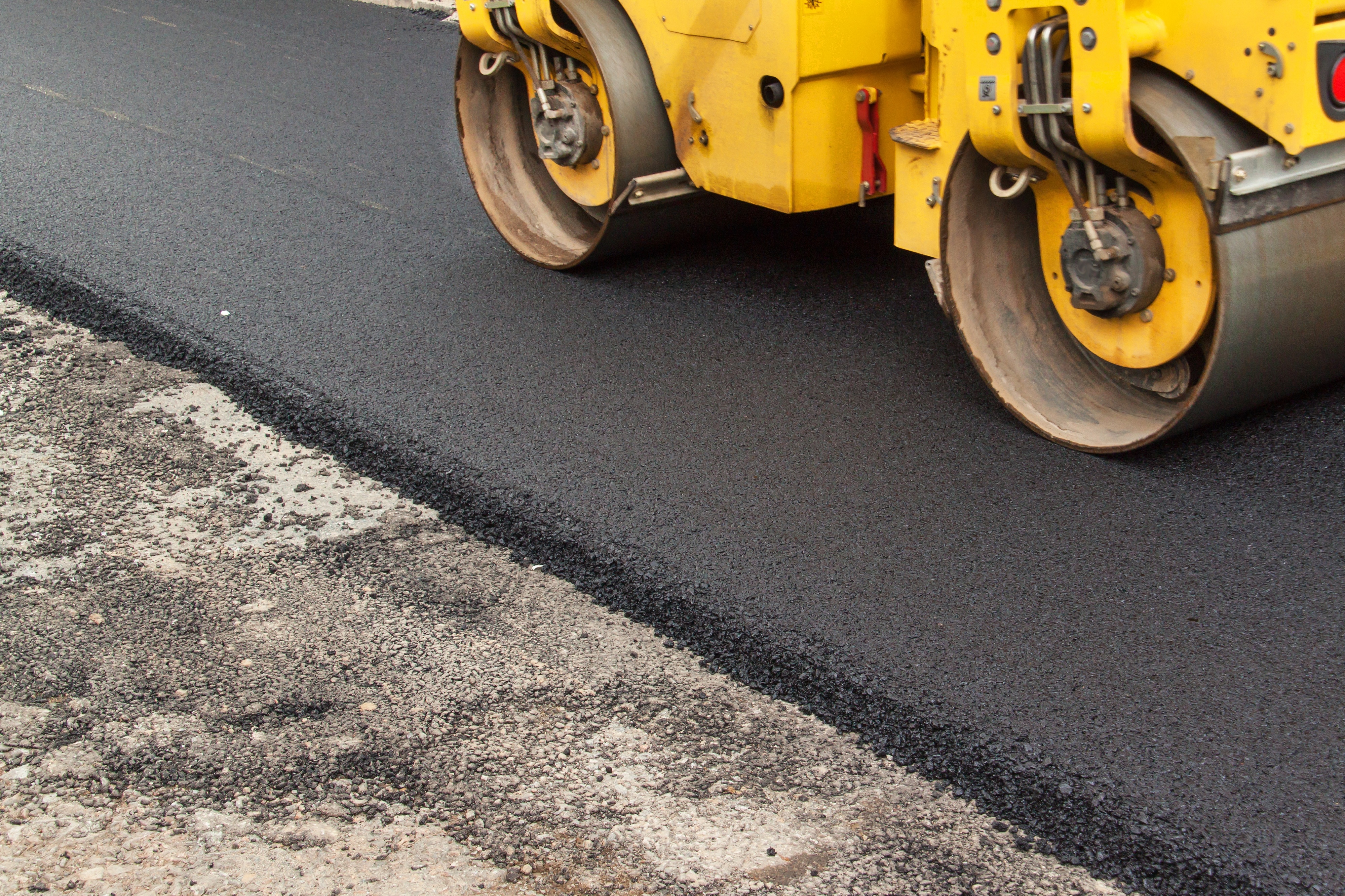 Yellow asphalt roller compacting fresh blacktop during road construction